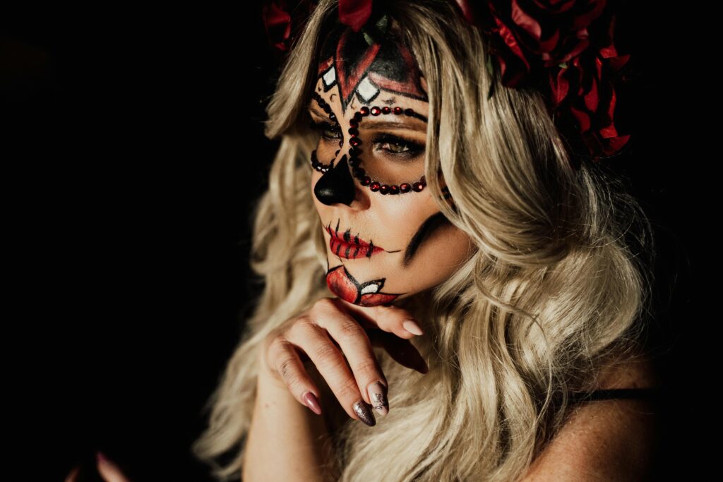 Blonde woman with intricate sugar skull makeup and red roses, perfect for Halloween.